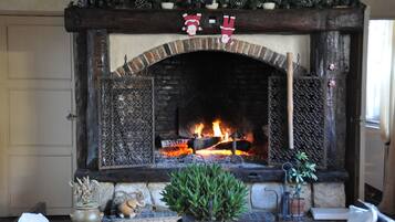 Une cheminée avec un foyer en briques, une étagère décorée d’ornements de Noël et un feu qui crépite à l’intérieur.
