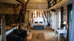 A bedroom with a large bed, a wooden coffee table, a desk with a chair, and a staircase leading to an upper level. - Le Logis De Gerberoy (Gerberoy)