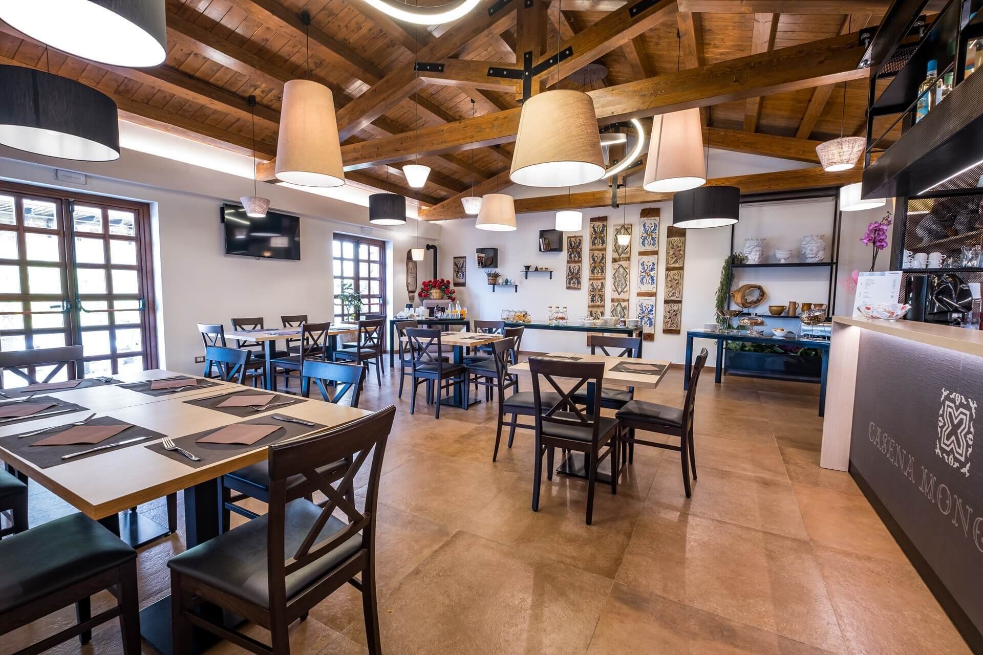 Un restaurante con vigas de madera, lámparas colgantes y una zona de bar con un panel de menú.