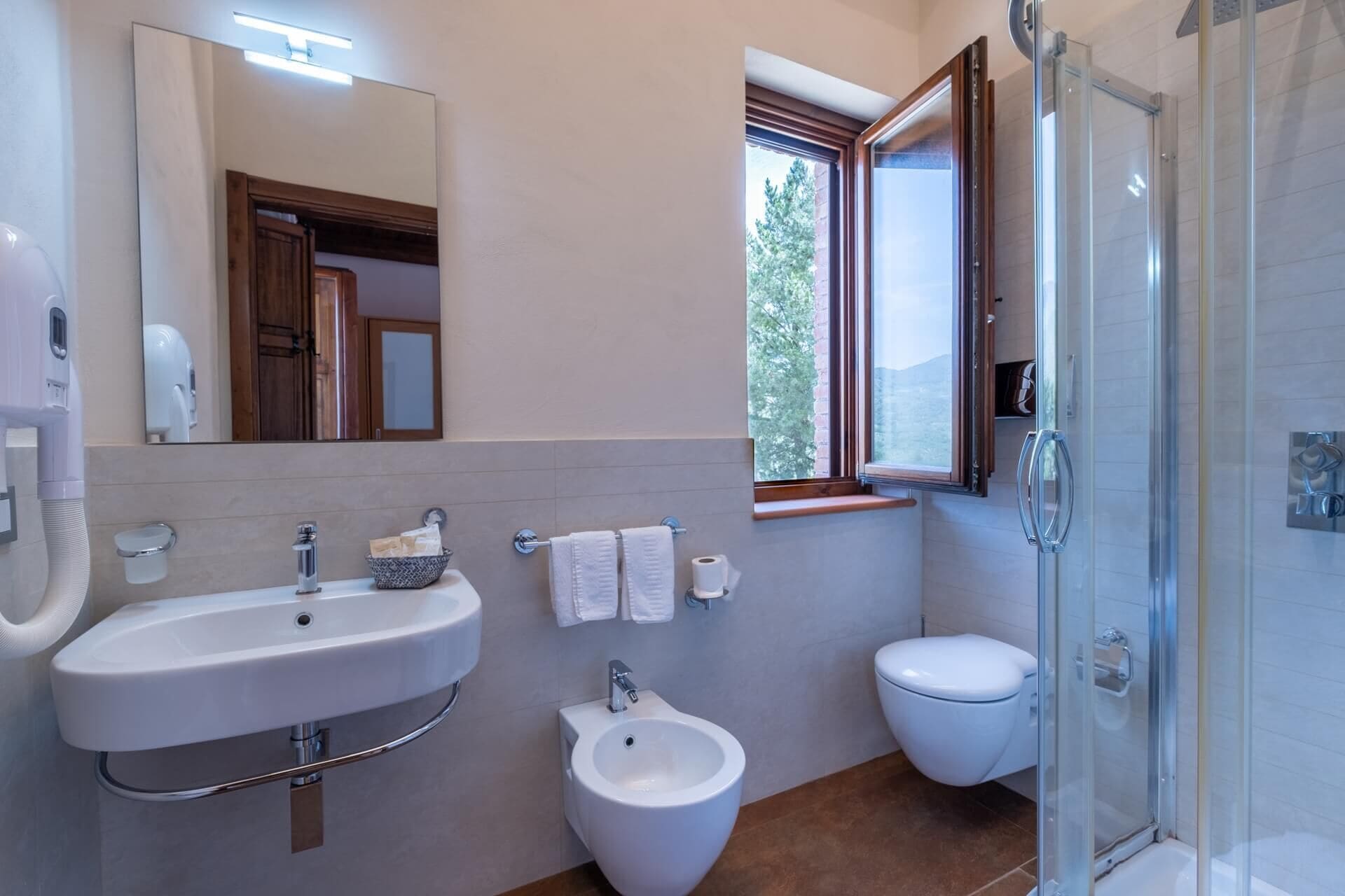 Un baño moderno con lavamanos, bidé, inodoro y ducha con mampara de vidrio.