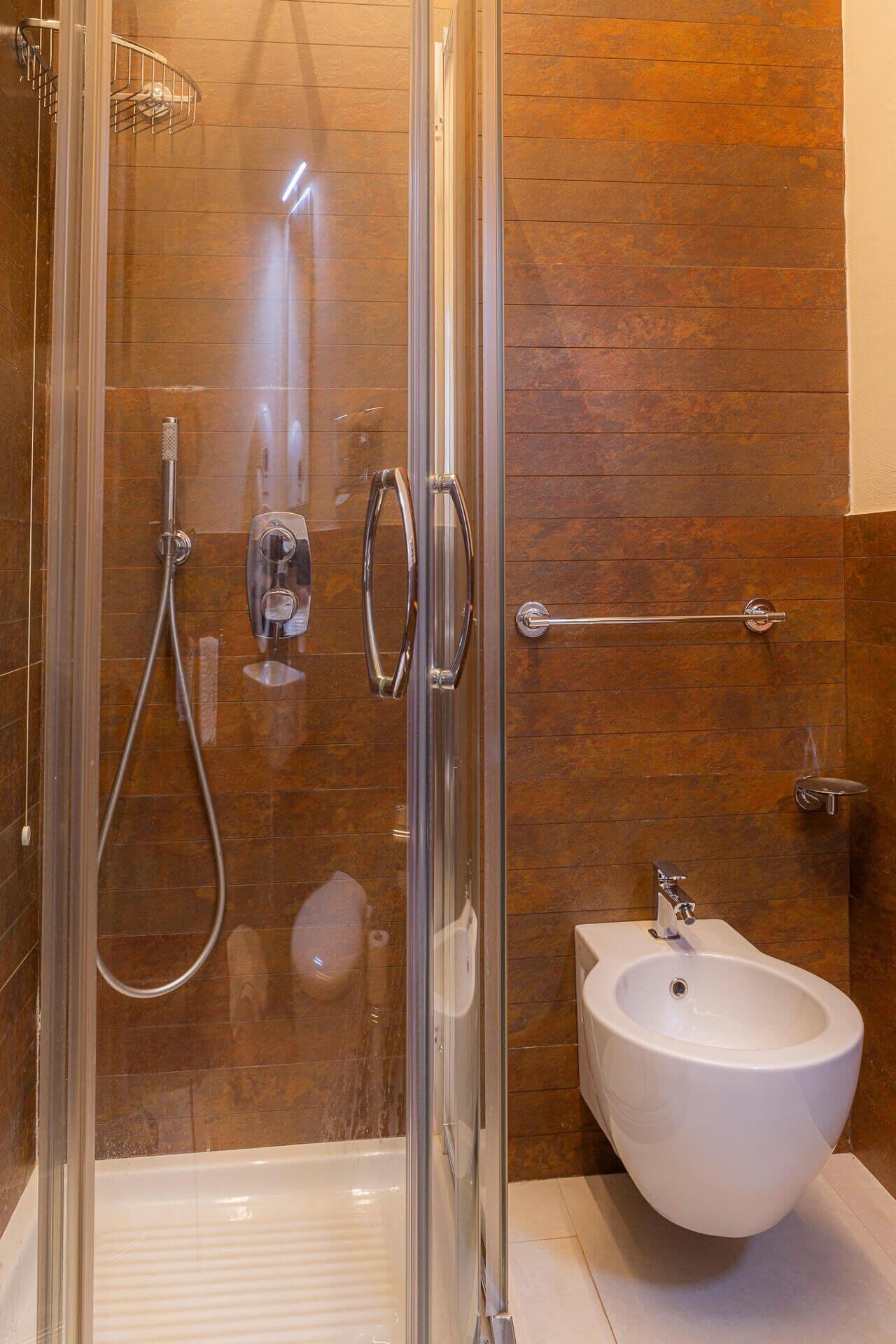 Ein modernes Badezimmer mit einer gläsernen Duschkabine, einem weißen Waschbecken auf Säule und Holzvertäfelung an den Wänden.