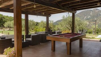 Mesa de billar en un patio exterior con mobiliario de mimbre y vistas a un paisaje montañoso.
