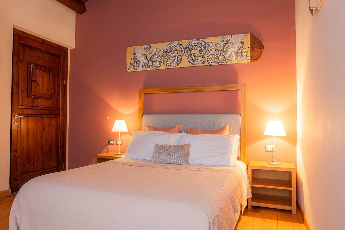A bedroom with a large bed, two bedside lamps, a wooden headboard, and a decorative panel above the bed.