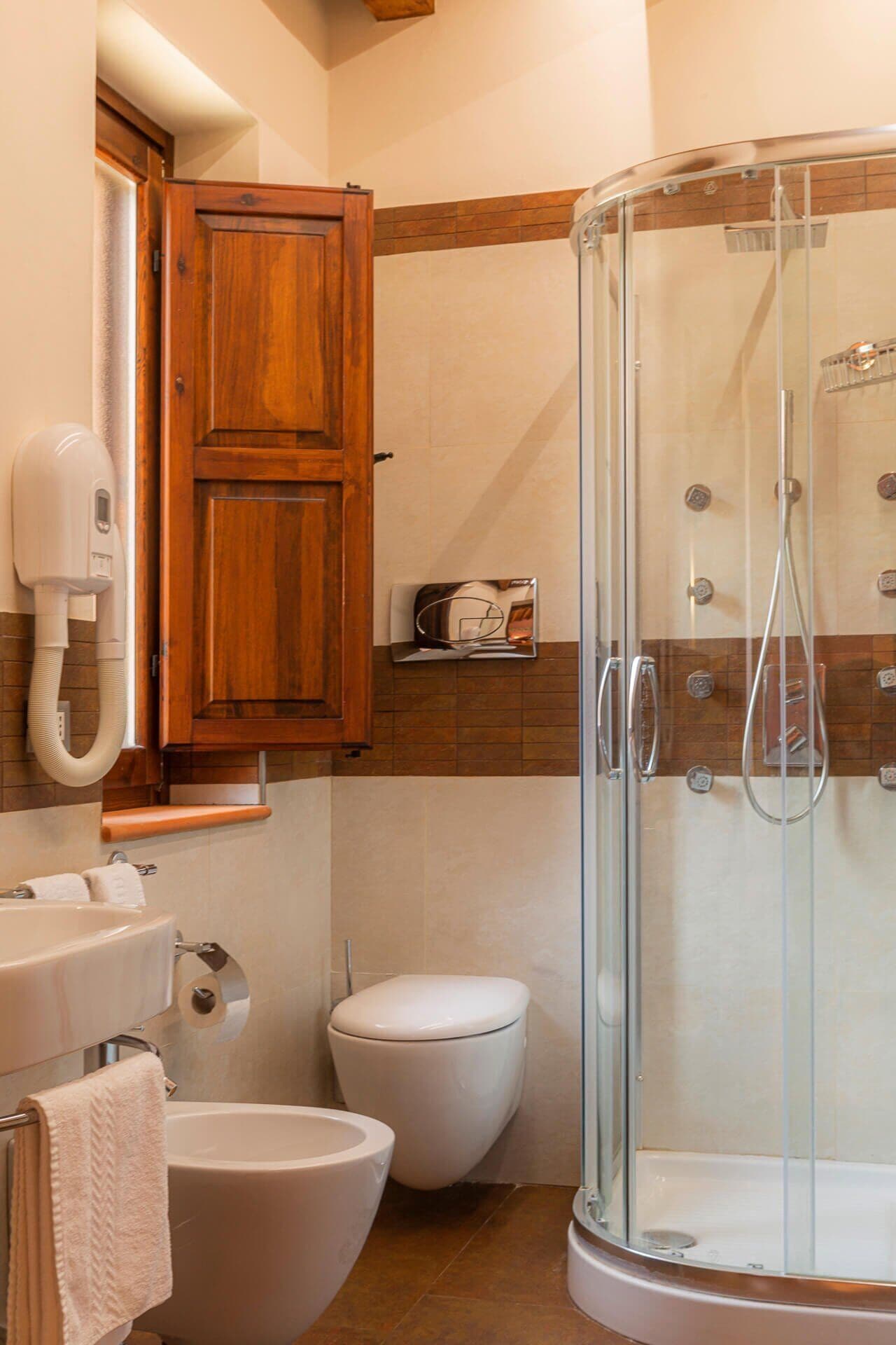 A bathroom with a shower, toilet, bidet, and wooden cabinets.