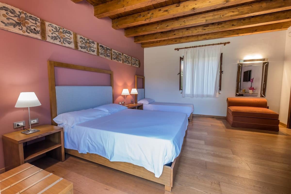 A bedroom with two beds, wooden flooring, a wooden ceiling, a nightstand with a lamp, and a small table.