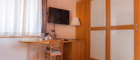 Una habitación pequeña con un escritorio de madera, una silla, un televisor montado en la pared, una lámpara y un armario con puerta corredera.