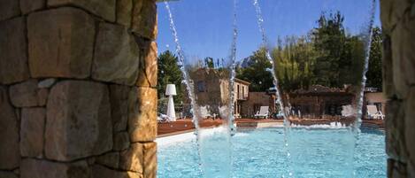 A stone-framed pool with clear water, surrounded by lounge chairs and a building with a tiled roof.