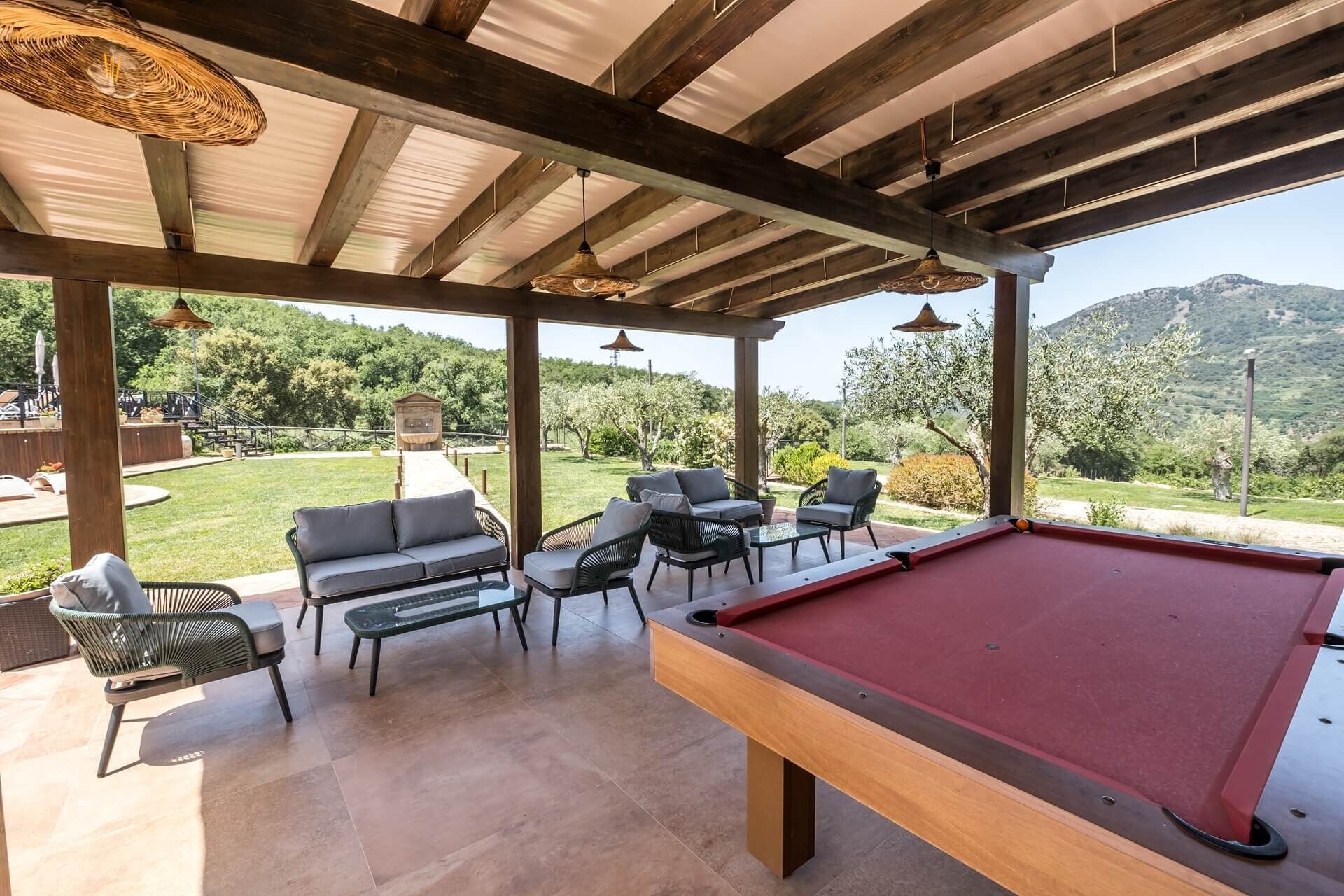 A pool table in a covered outdoor area with seating and a view of a mountainous landscape.