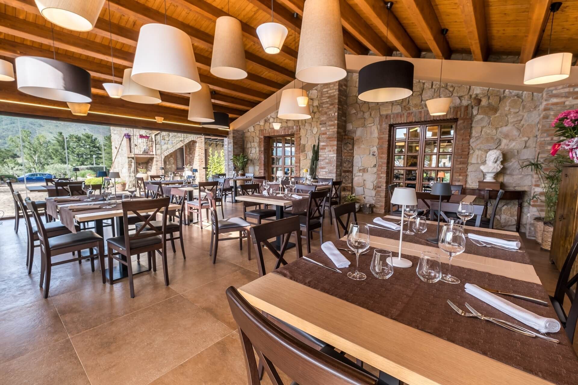 Un restaurante con vigas de madera y paredes de piedra, que cuenta con varias mesas y sillas, y lámparas colgantes.