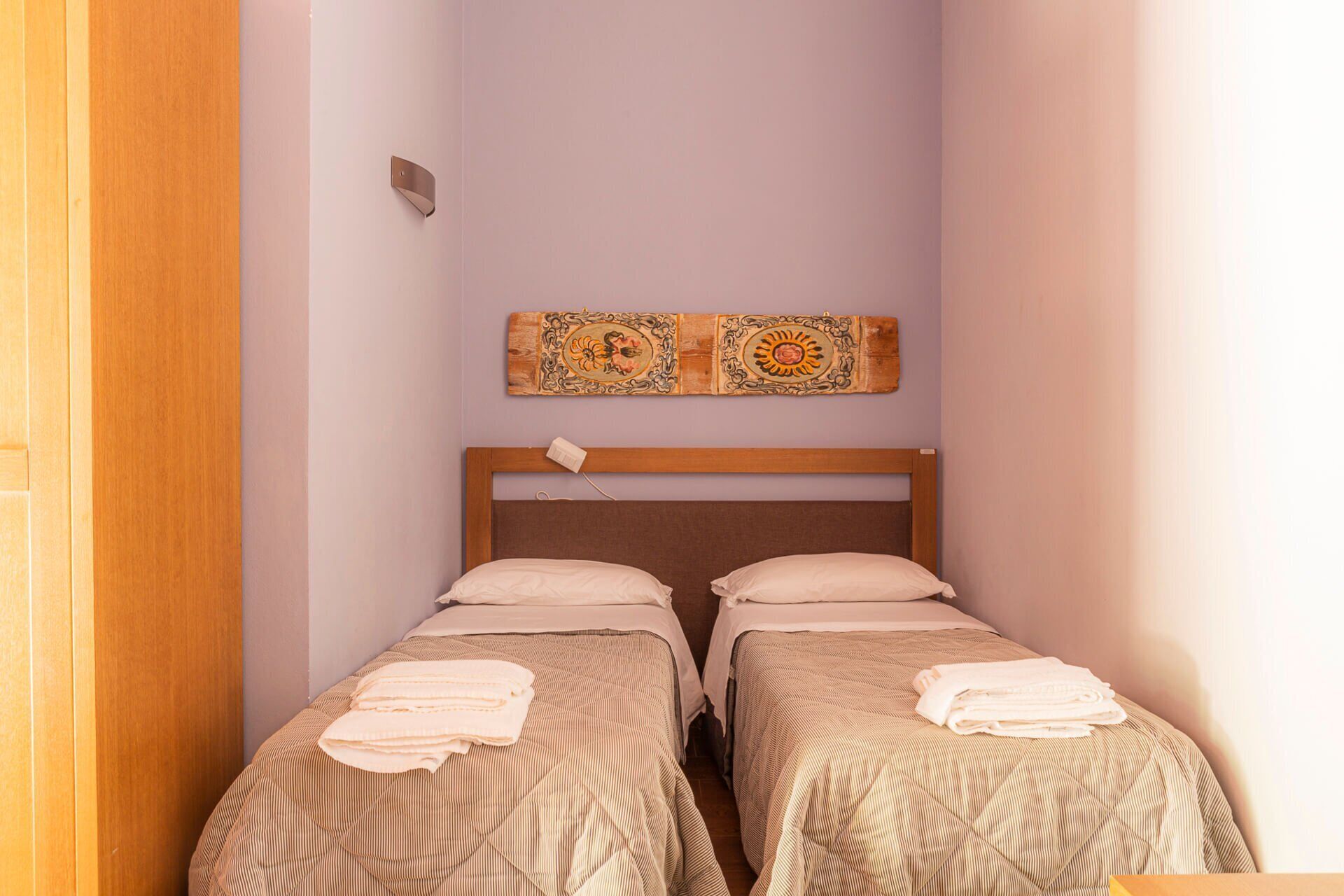 A small room with two single beds, a wooden headboard, and a wall-mounted light fixture.