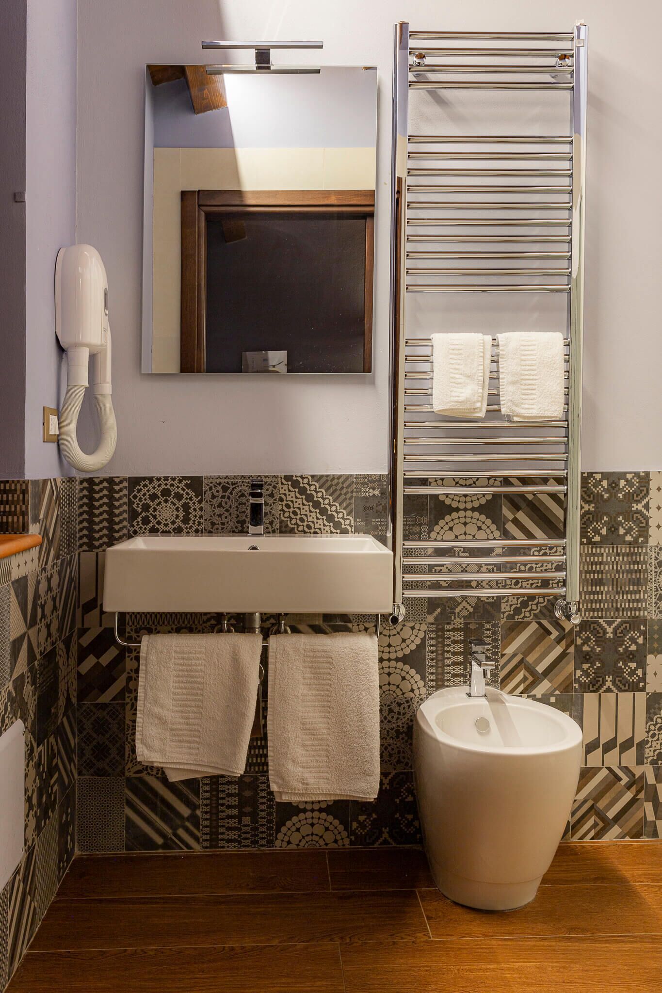 A bathroom with a sink, mirror, towel rack, and patterned tiles.