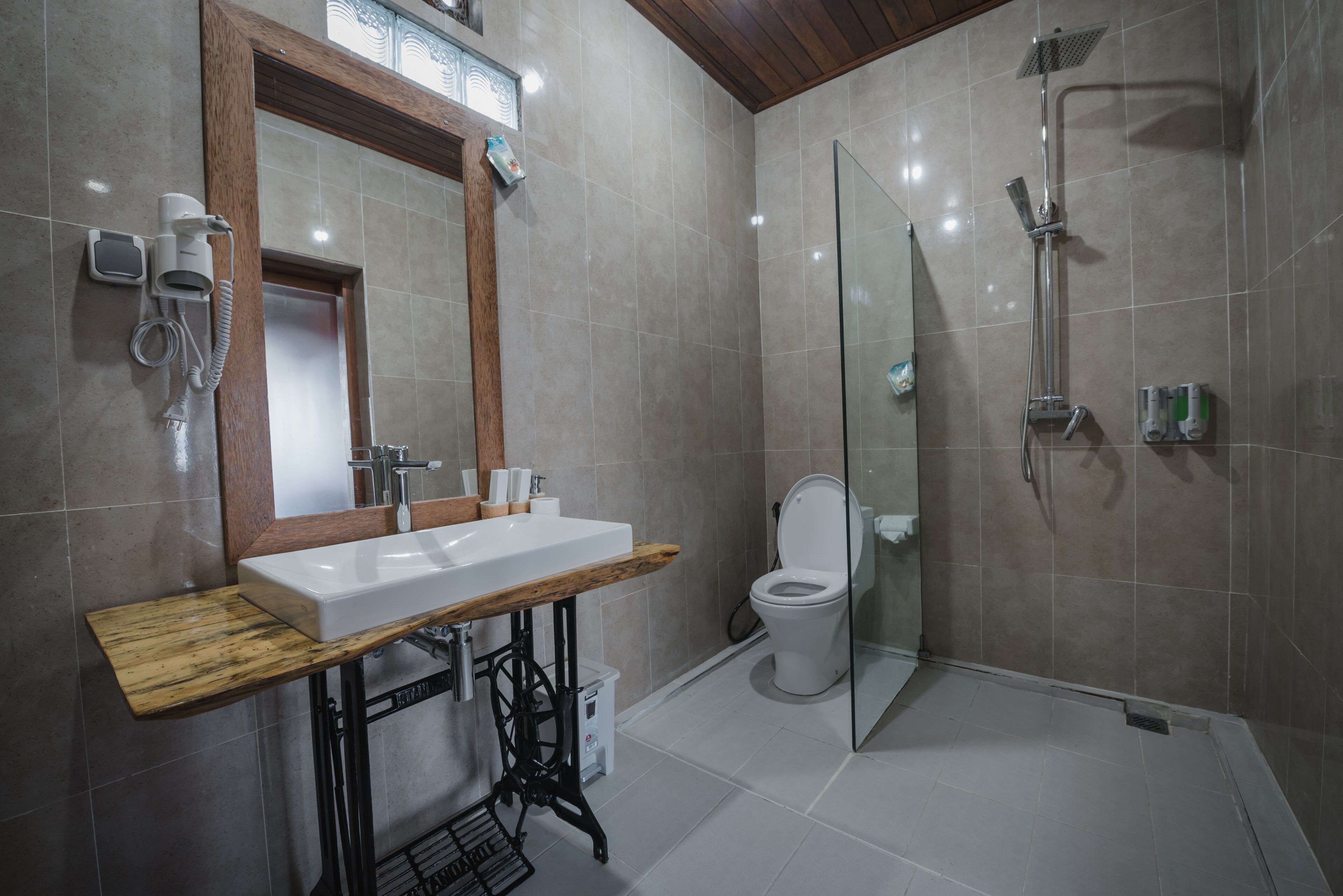 A bathroom with a wooden vanity, a white sink, a mirror, a toilet, and a shower area.