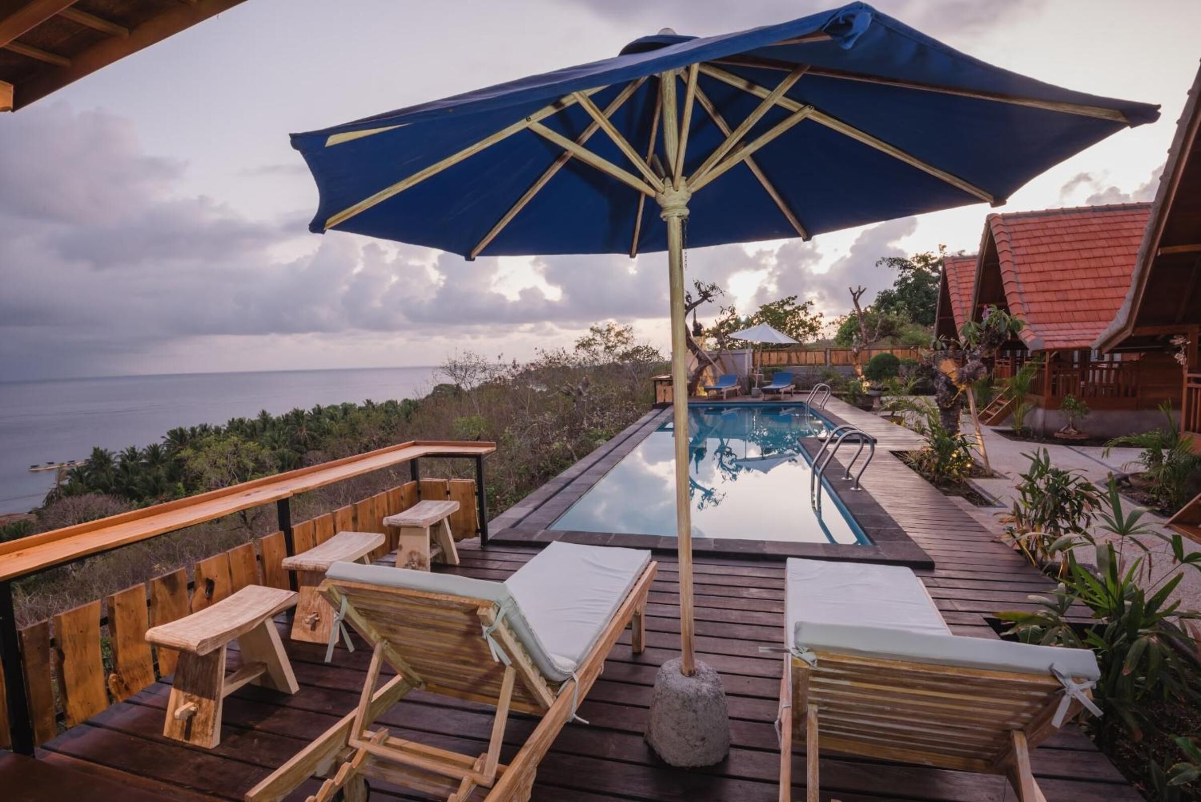 Um deck de madeira com espreguiçadeiras e piscina, com vista para o mar.
