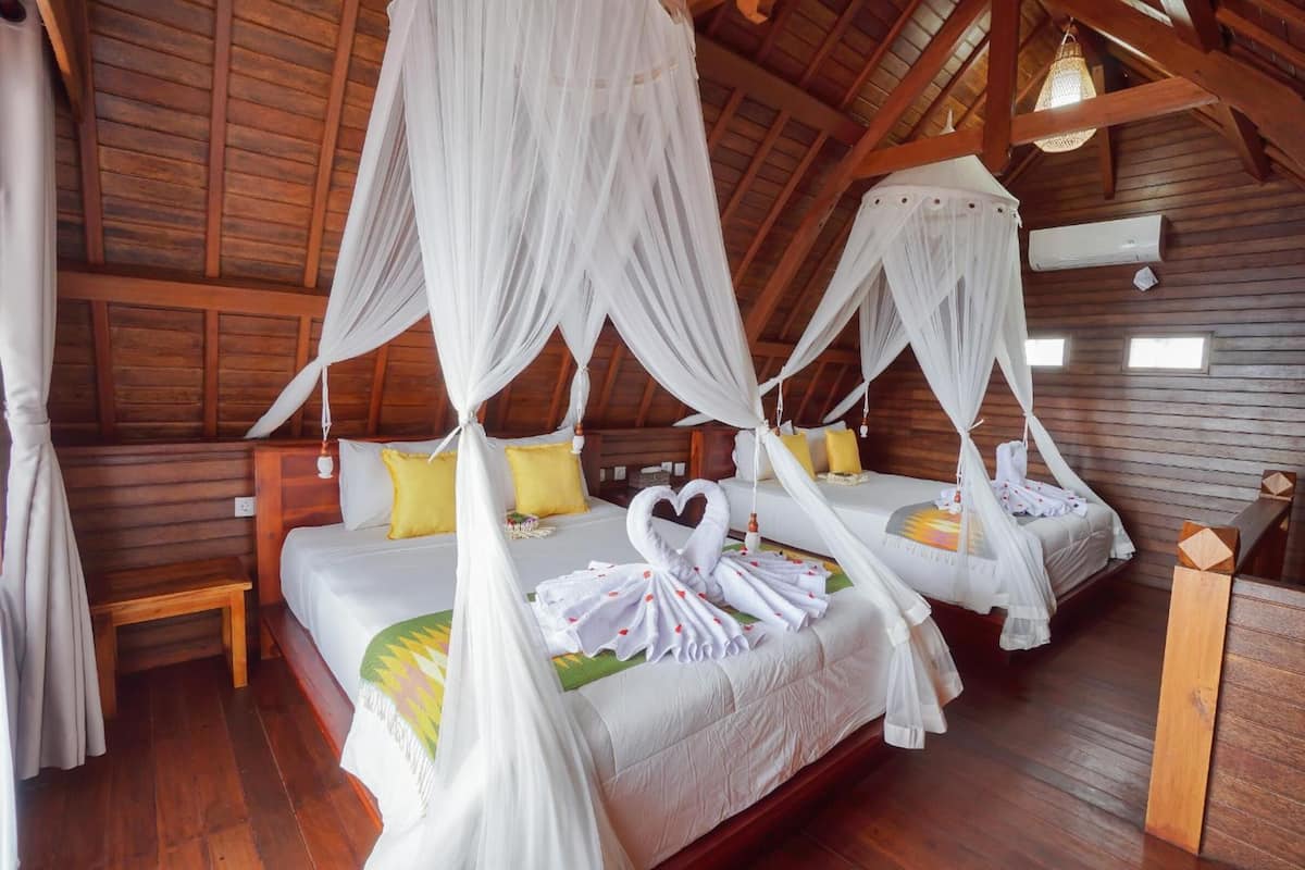 A room with four beds, each with a canopy bedspread and a heart-shaped towel arrangement.