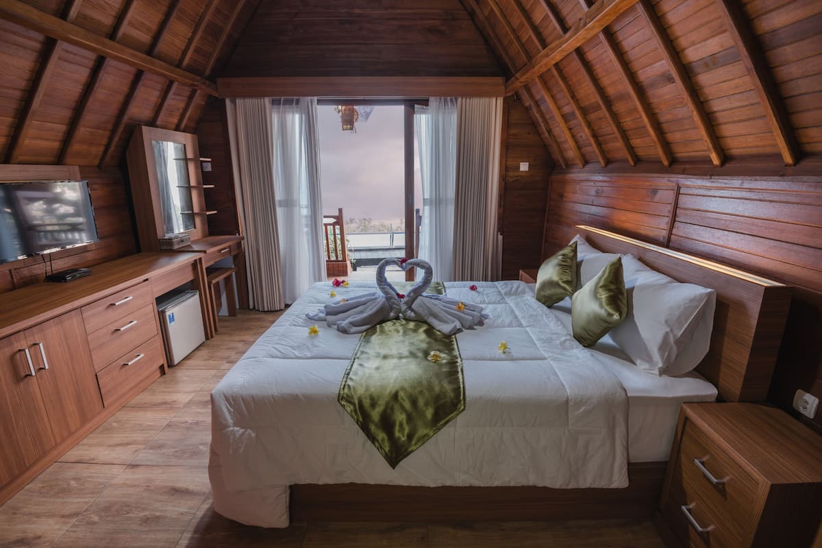 A bedroom with a wooden ceiling, a bed with a green runner, a TV, and a window with curtains.