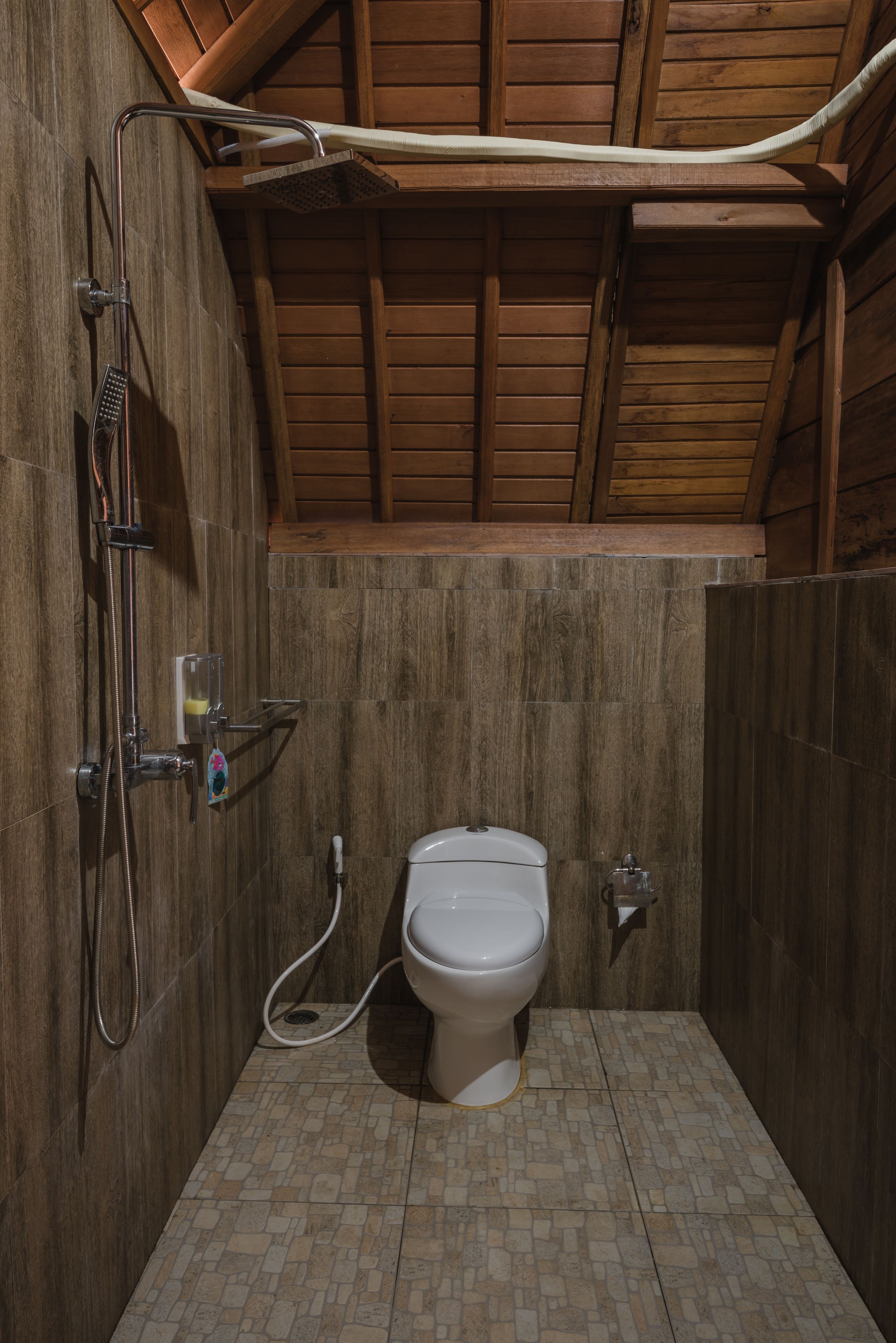 A small, wooden-walled bathroom with a shower, toilet, and tiled floor.