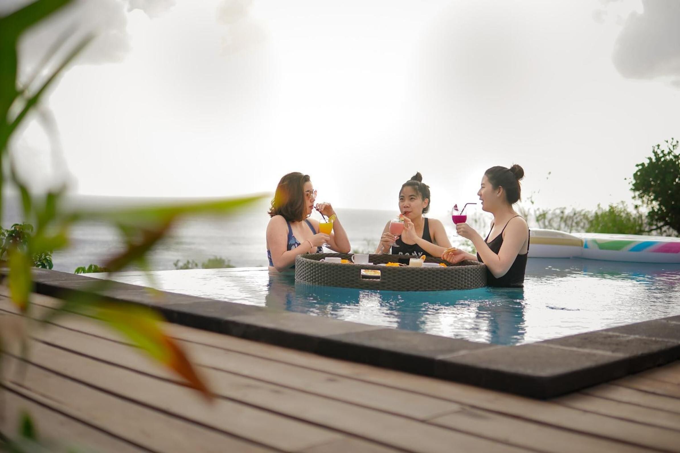 Three people sitting at a round table in a poolside setting with a view of the sea.