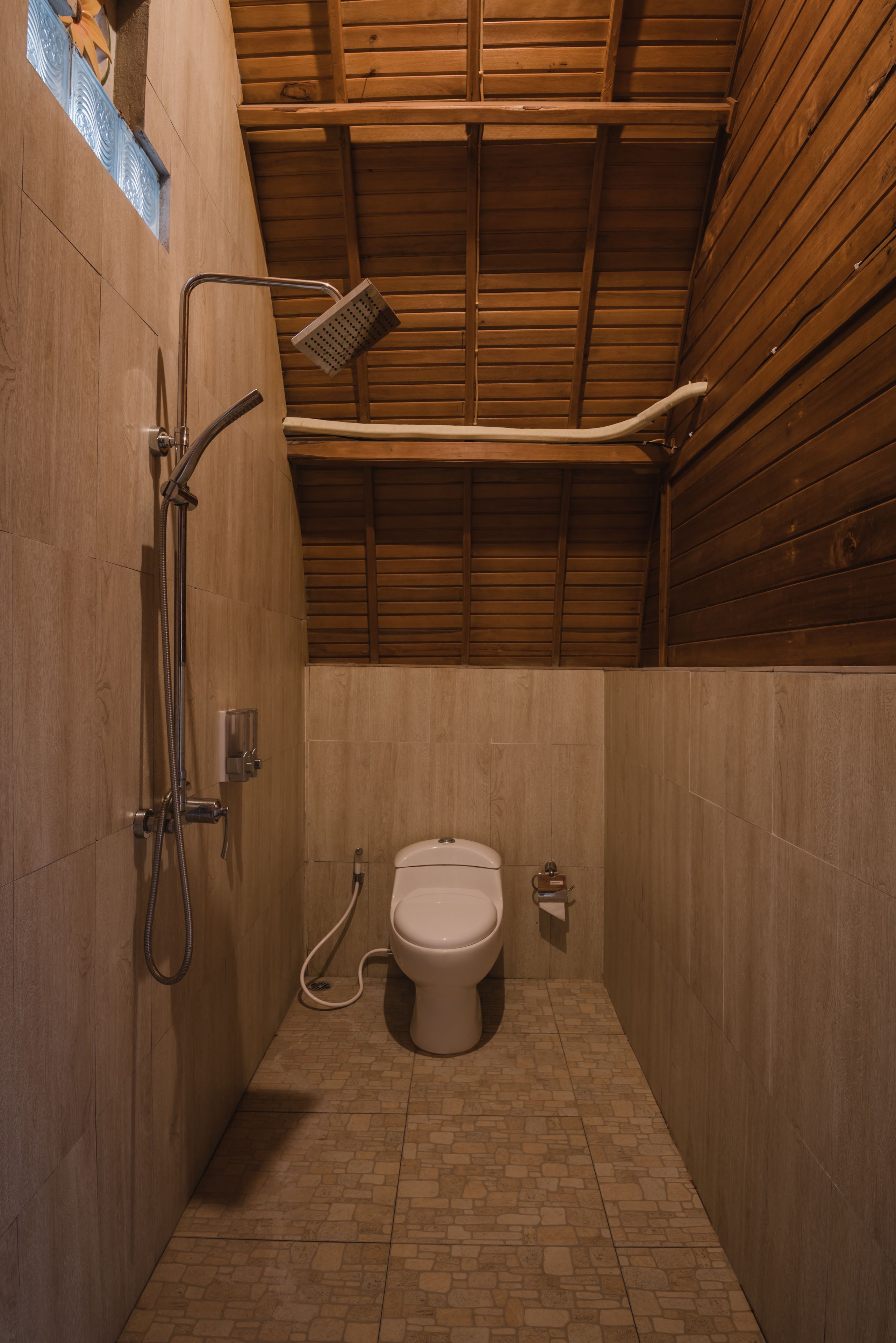 Un baño pequeño y cerrado con ducha, inodoro y techo de madera.