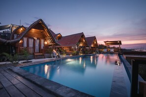 A poolside area with wooden chalets, a swimming pool, and a deck with lounge chairs.