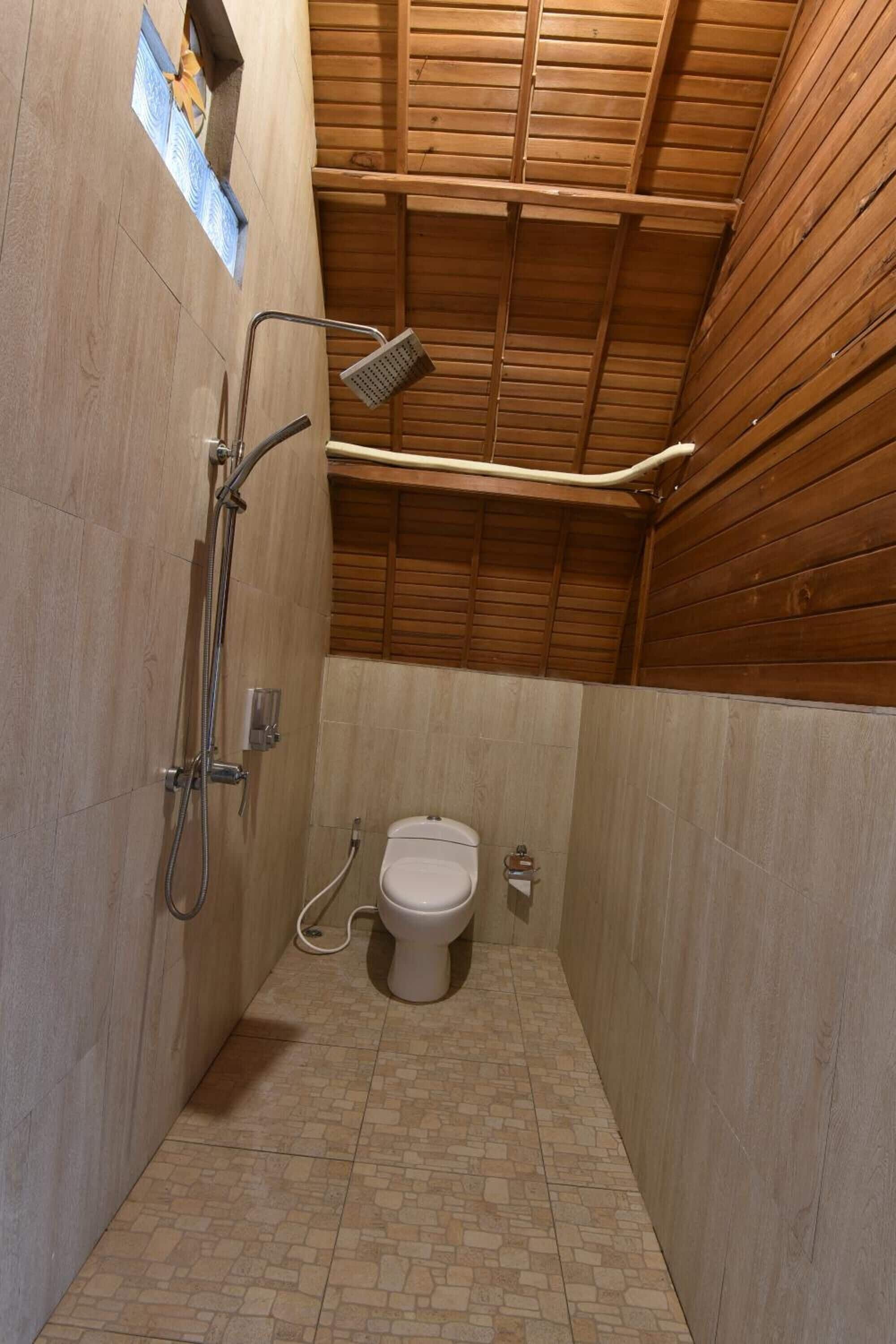 Un baño pequeño y cerrado con techo de madera, ducha e inodoro.