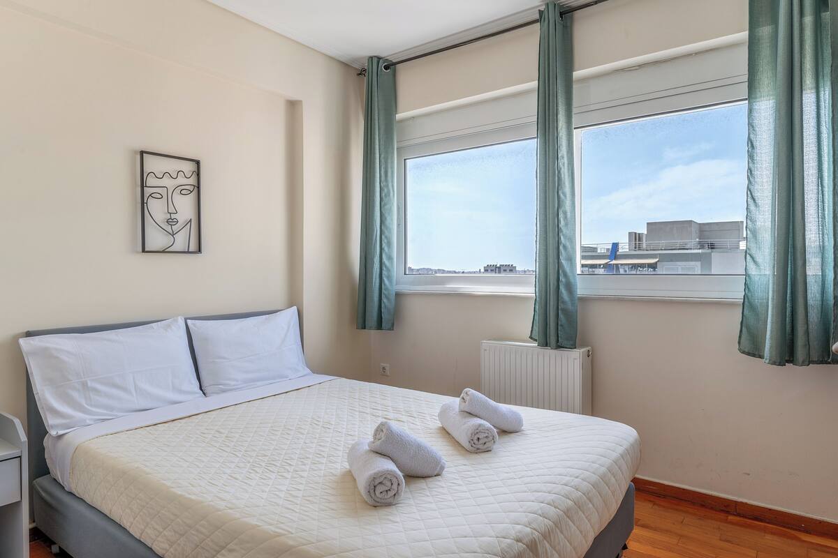 Una habitación de hotel con cama, radiador, ventana con cortinas y una obra de arte colgada en la pared.