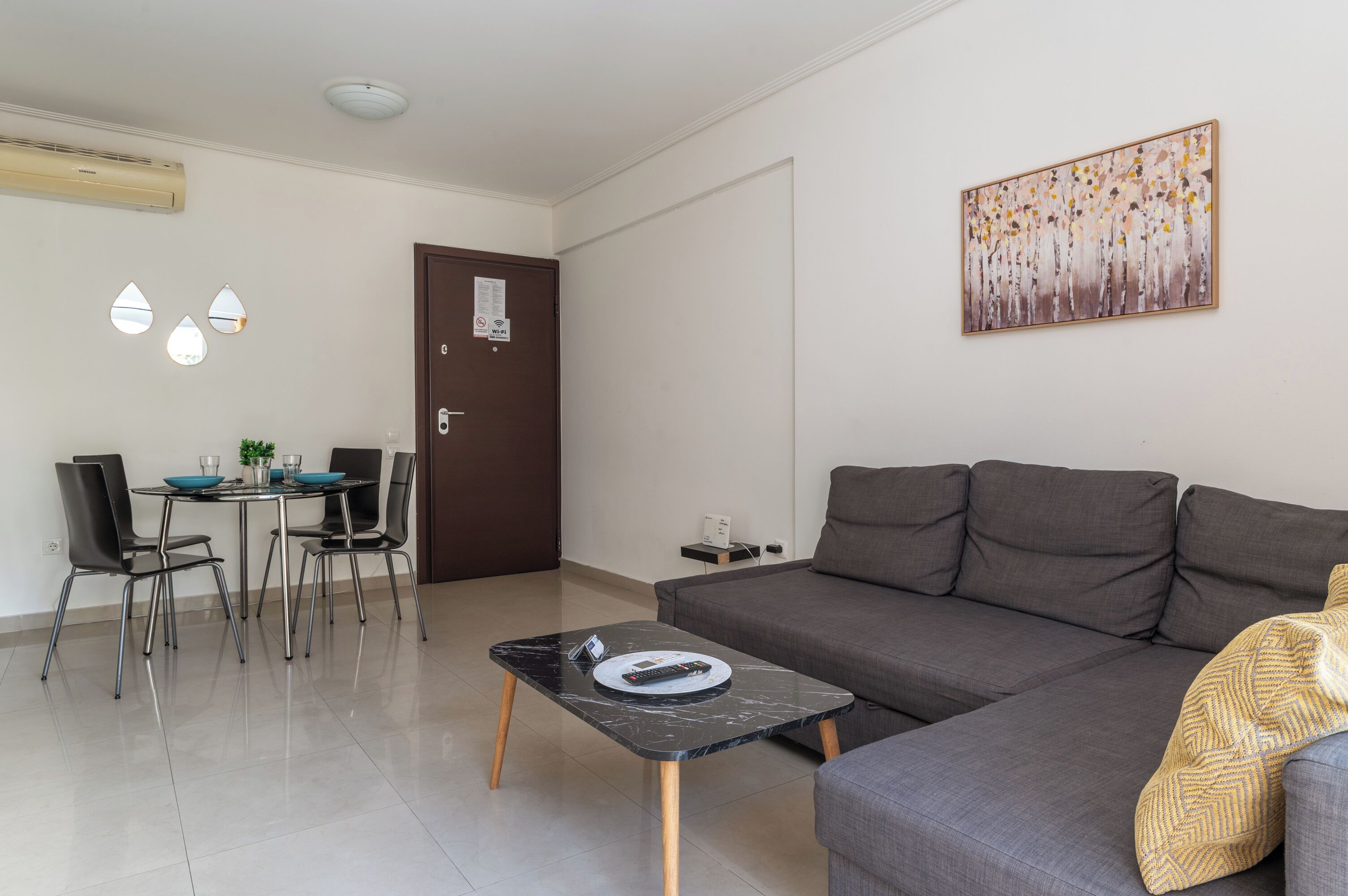 A modern living room with a grey sofa, a black coffee table, a dining table with chairs, and a painting on the wall.