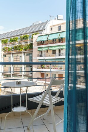 A balcony with a table and two chairs, overlooking a residential area with multiple buildings. - Elvita Apartments 2 (Athens)