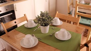 Una mesa de comedor de madera con cuatro tazas y platillos blancos, un posavasos verde y una planta en maceta.