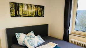 Una camera da letto con un letto, una finestra con tende, un termosifone e un quadro a tema boschivo.