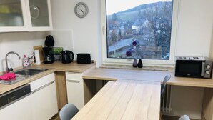 Una cucina moderna con un tavolo di legno, due sedie, un lavandino, una macchina del caffè, un tostapane, una sveglia e una finestra con vista su una città.