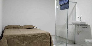 A room with a bed, a glass shower enclosure, and a white sink. - Suítes Olinda (Cabo Frio)