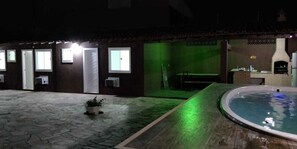 A nighttime outdoor pool area with a stone patio, a hot tub, and a brick oven. - Suítes Olinda (Cabo Frio)
