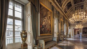 An opulent room with a grand chandelier, a large mural, and a view of the city through large windows. - Donna Lena Relais (Naples)