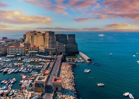 Een kustplaats met een historisch kasteel, een jachthaven vol boten en een rotsachtige waterkant.