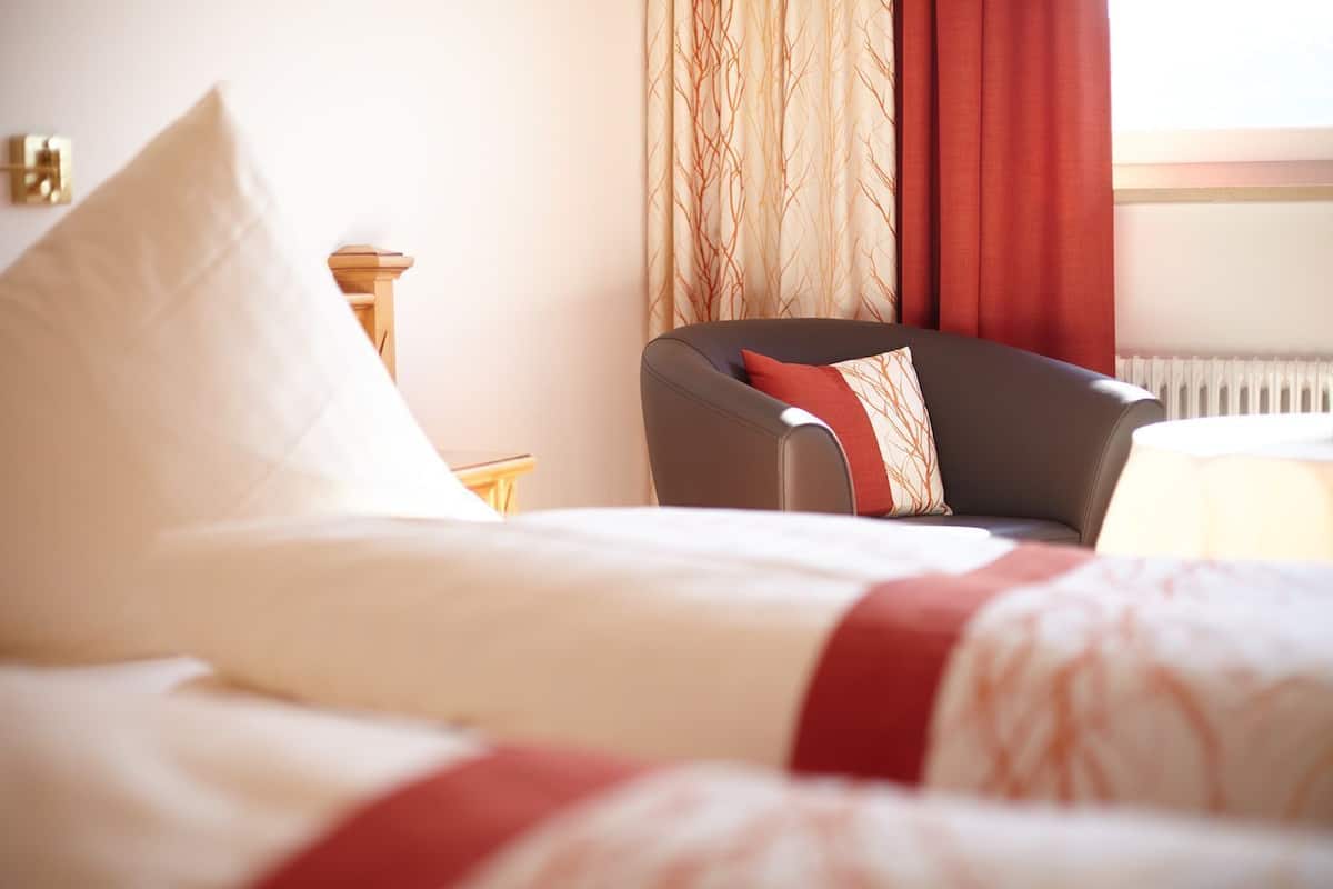 Een hotelkamer met een bed, een stoel, een nachtkastje en een raam met gordijnen.