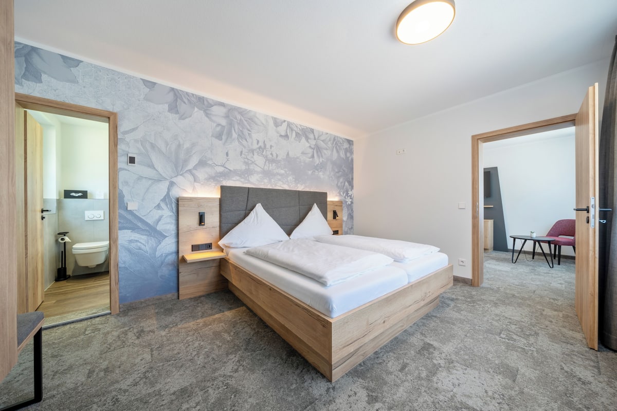 Een moderne slaapkamer met een houten bed, een nachtkastje en een wand met een groot bloemenmotief.