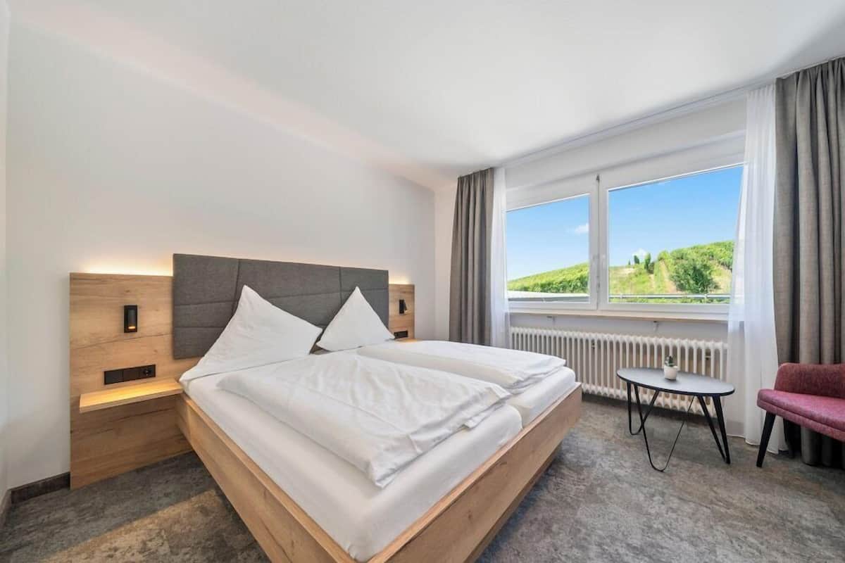 Een hotelkamer met een bed, nachtkastjes, een klein tafeltje, een stoel en een raam met uitzicht.