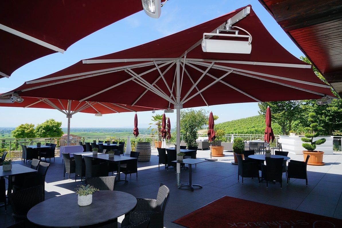 An outdoor patio with tables and chairs, red umbrellas, and a view of the landscape.