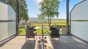 A covered outdoor seating area with a table and chairs, overlooking a scenic landscape with fields and trees.