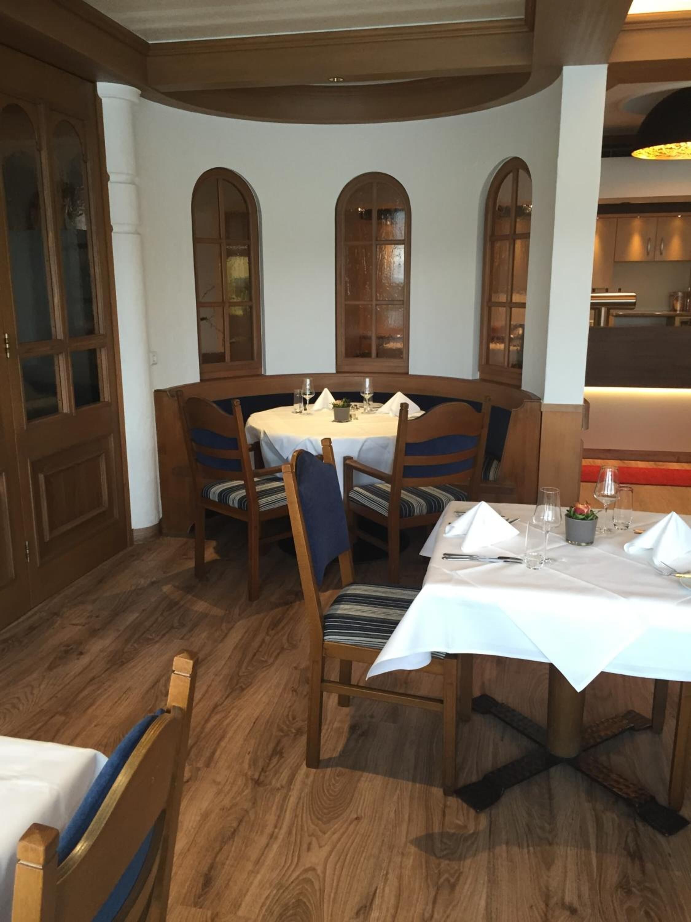Un comedor con una mesa redonda para cuatro personas, sillas de madera con cojines azules y un mantel blanco.