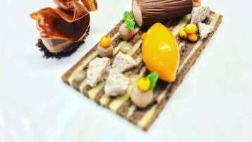 A dessert with various components including a chocolate-covered item, a log-shaped piece, and small round elements.