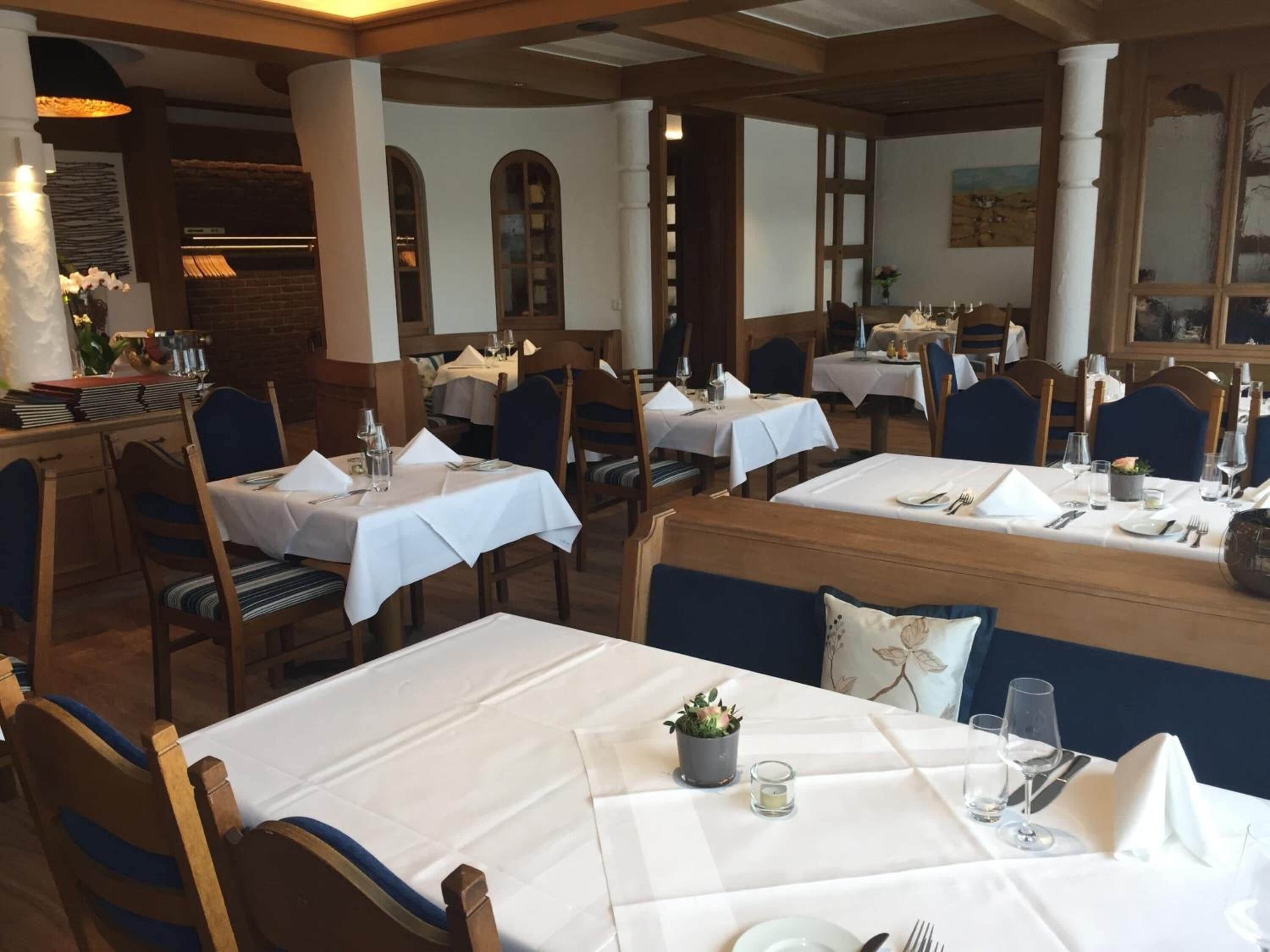 Un restaurante con varias mesas dispuestas para comer, con manteles blancos y sillas de madera.