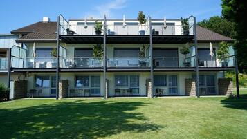 A modern two-story house with a balcony on each floor, stone pillars, and a well-maintained lawn.