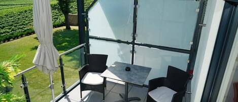 En balkon med to fletstole og et bord, med udsigt over en vingård.