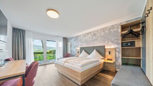 A modern hotel room with a large bed, a dining table, and a view of the outdoors.