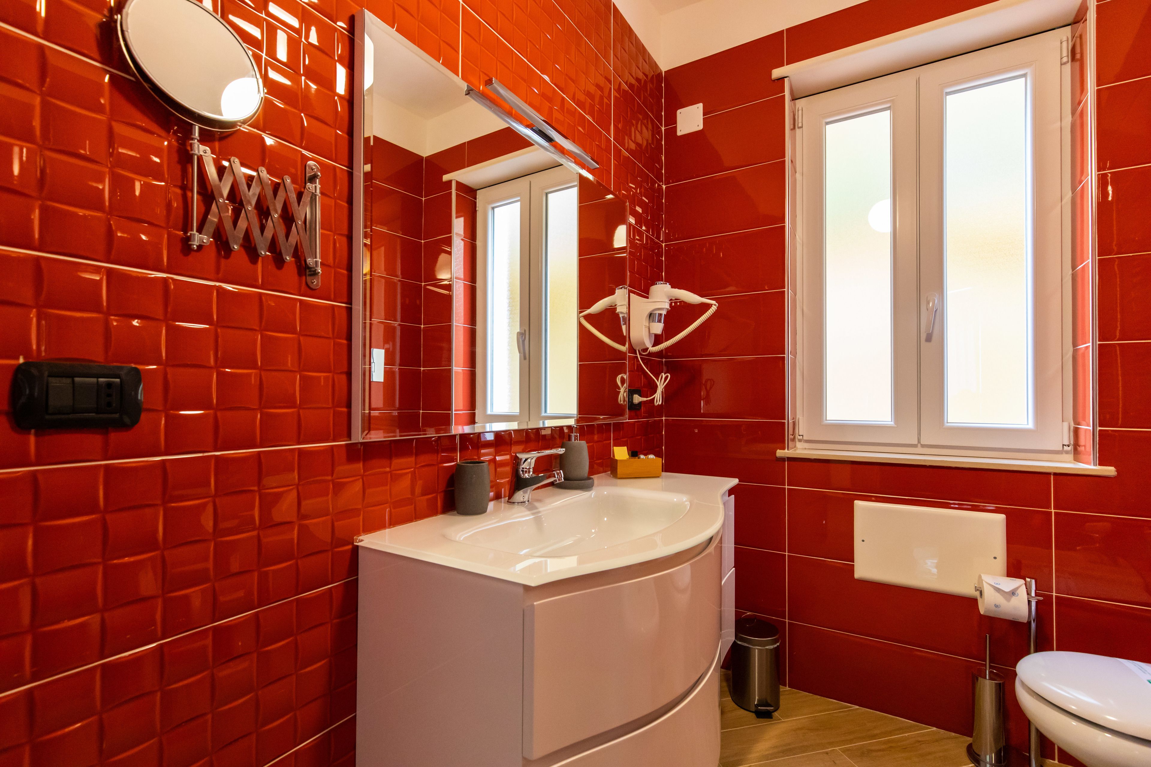Ein Badezimmer mit roten Fliesenwänden, einem weißen Waschbecken, einem Spiegel und einem Fenster.