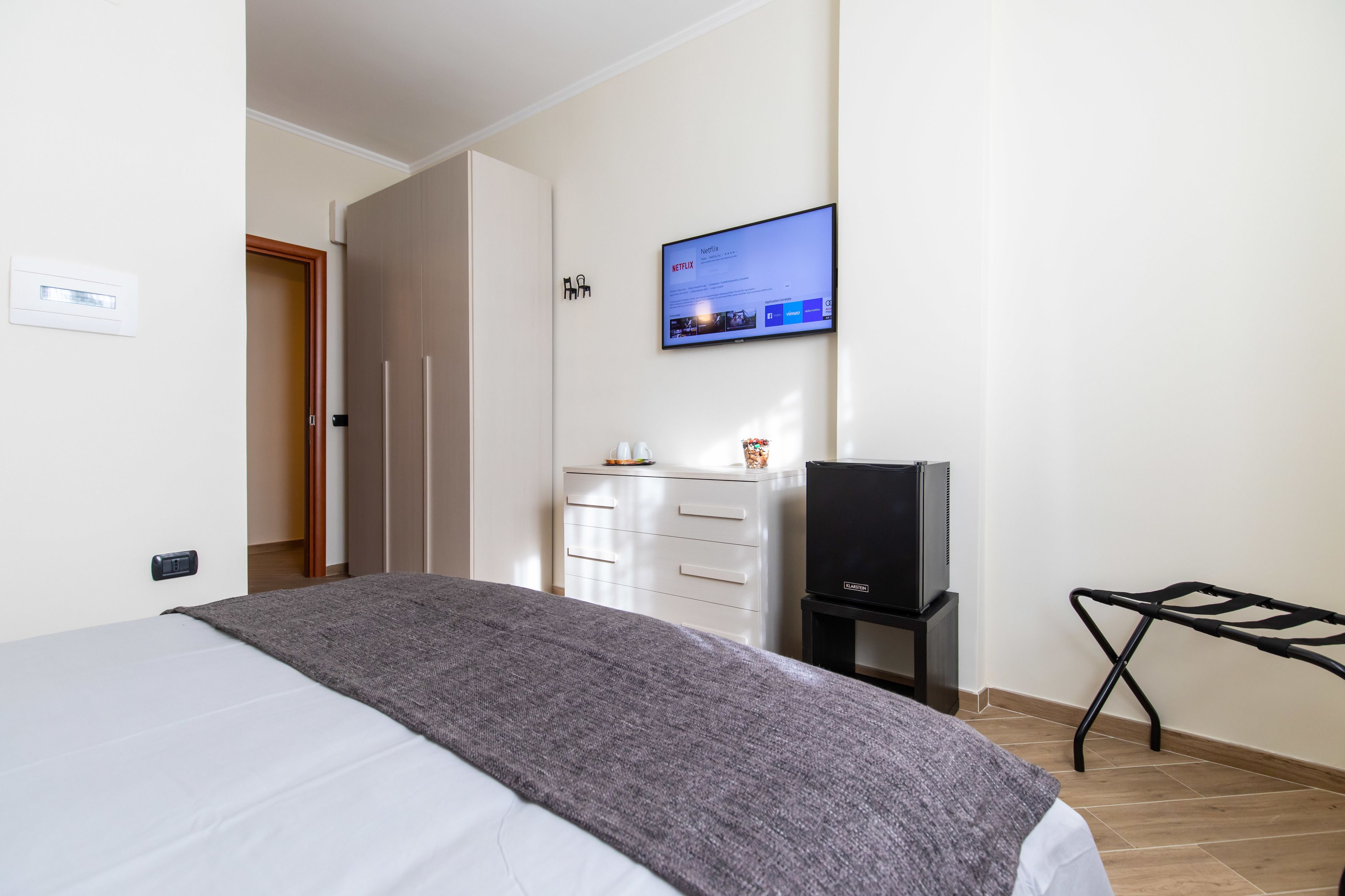 A hotel room with a bed, a TV mounted on the wall, a dresser, and a small table with a TV stand.
