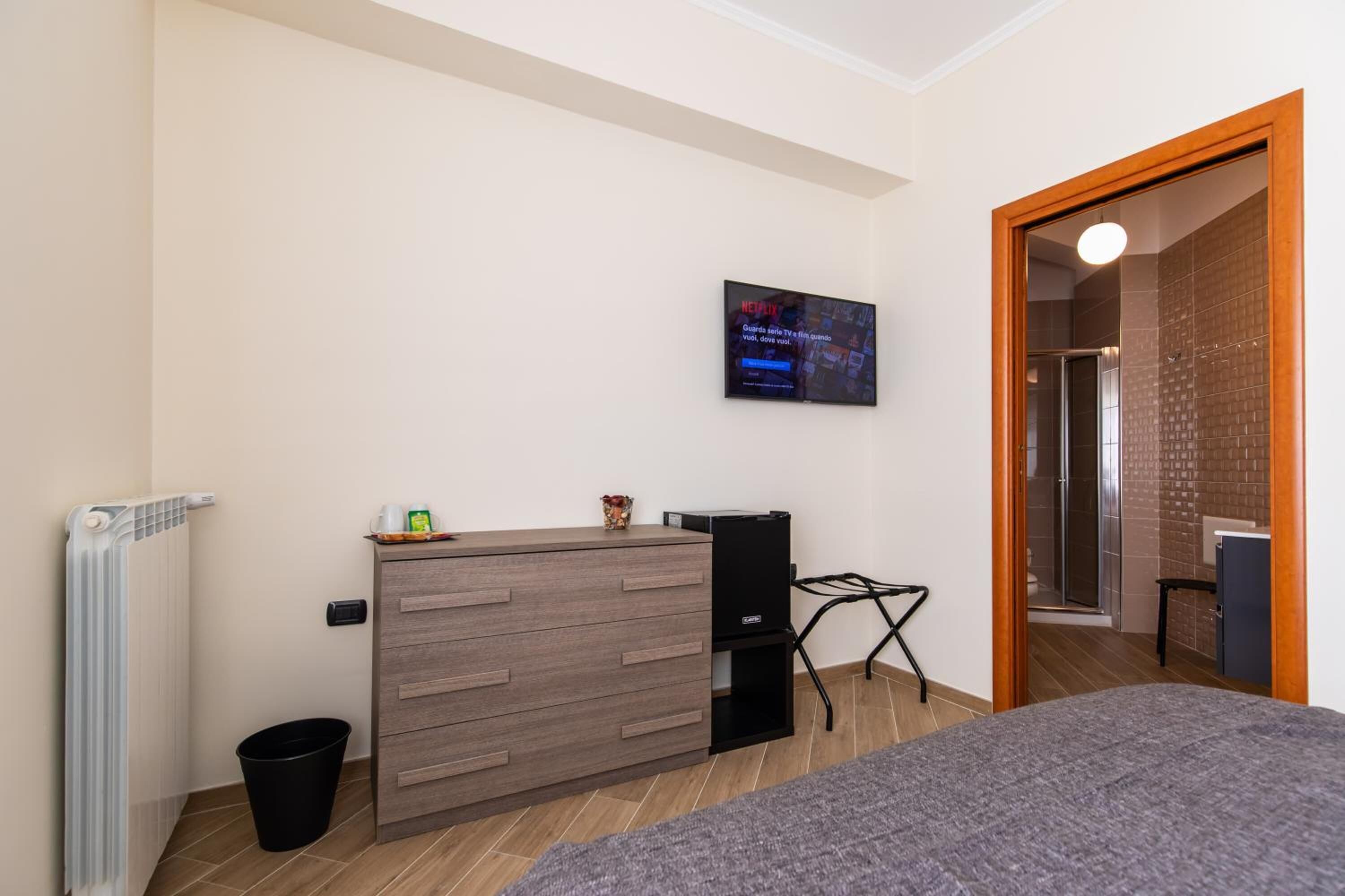 Een moderne slaapkamer met een houten dressoir, een aan de muur bevestigde televisie, een klein bureau en een bed.