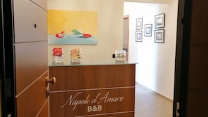 Una recepción con letrero de 'Napoli d'Amare B&B', un cuadro abstracto de colores y fotografías enmarcadas en la pared.