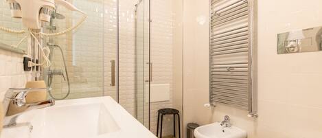 A modern bathroom with a large white sink, a glass shower enclosure, a bidet, and a towel rack.